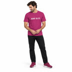 Full-body man wearing the berry JUST SI IT. t-shirt with white chest lettering and matching trainers, hands clasped at his waist on a white background.