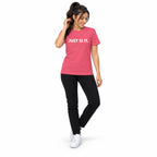 Full-body woman wearing the charity pink JUST SI IT. t-shirt with white chest lettering and white trainers, touching her hair on a white background.