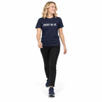 Full-body blonde woman wearing the navy JUST SI IT. t-shirt with white chest lettering and navy trainers, stepping forward on a white background.