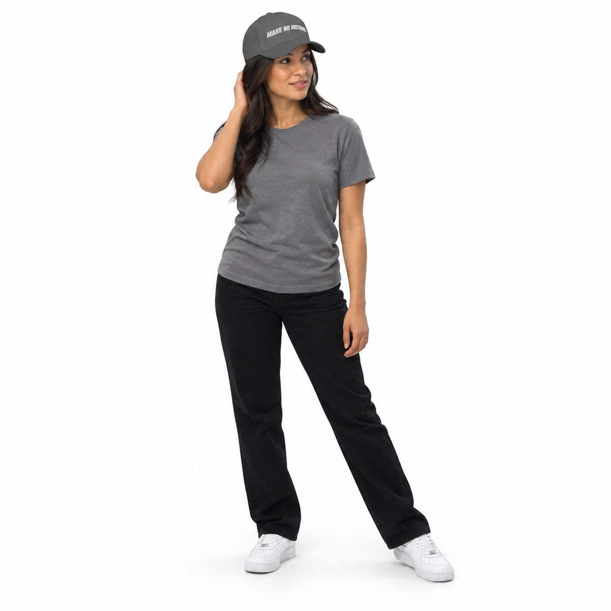 Full-body model wearing the grey MAKE NO MISTAKES. embroidered cap with a matching grey T-shirt and white shoes, touching her hair on a white background.