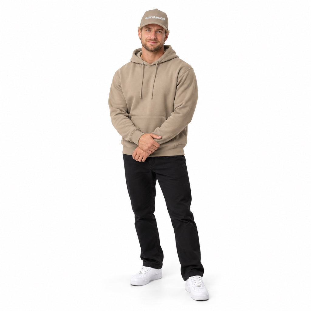 Full-body blonde model wearing the khaki MAKE NO MISTAKES. embroidered cap with a matching khaki hoodie and white shoes, hands resting at his waist on white.