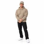Full-body blonde model wearing the khaki MAKE NO MISTAKES. embroidered cap with a matching khaki hoodie and white shoes, hands resting at his waist on white.