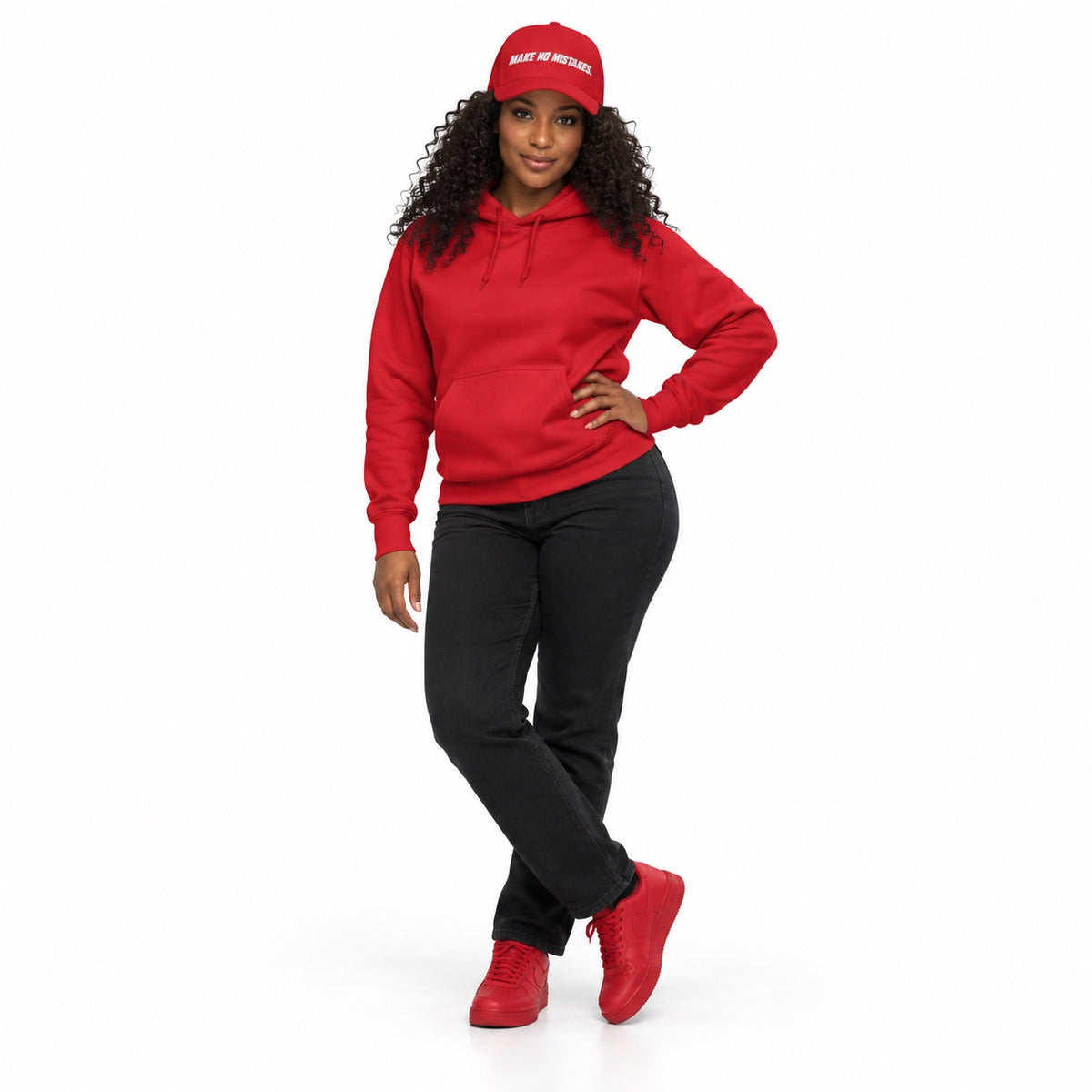 Full-body model wearing the red MAKE NO MISTAKES. embroidered cap with matching red hoodie and shoes, one hand on her hip and ankles crossed on white.