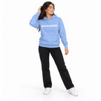 Full-body model wearing the Carolina blue MAKE NO MISTAKES. hoodie with white chest print, touching her hair and looking aside on a plain white background.