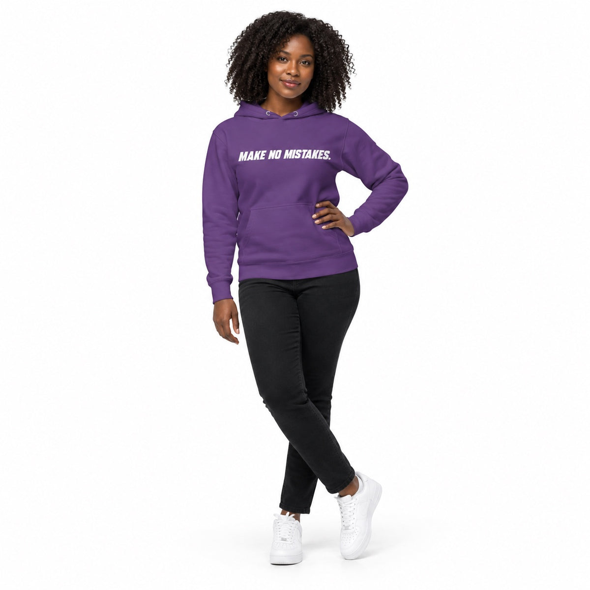 Full-body model wearing the purple MAKE NO MISTAKES. hoodie with white chest print, one hand on her hip and ankles crossed on a plain white background.