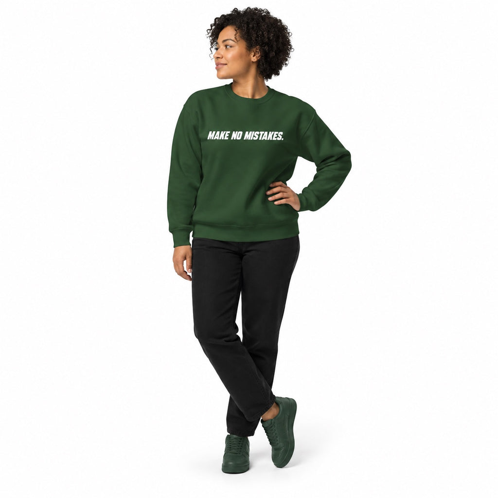 Full-body woman wearing the forest green MAKE NO MISTAKES. sweatshirt with white chest print and matching trainers, hand on hip on a white background.