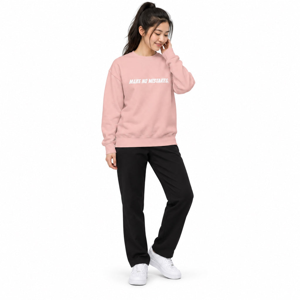 Full-body woman wearing the light pink MAKE NO MISTAKES. sweatshirt with white chest print, touching her hair with white trainers on a white background.