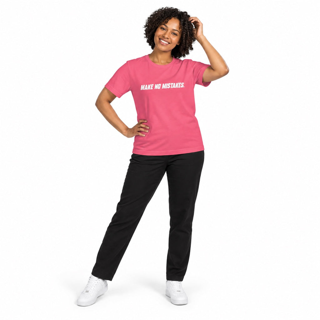 Full-body model wearing the charity pink MAKE NO MISTAKES. T-shirt with white chest print, smiling with one hand touching her hair and the other on her hip on a white background.