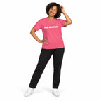 Full-body model wearing the charity pink MAKE NO MISTAKES. T-shirt with white chest print, smiling with one hand touching her hair and the other on her hip on a white background.