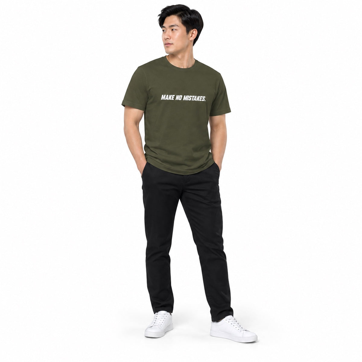 Full-body model wearing the military green MAKE NO MISTAKES. T-shirt with white chest print, standing with both hands in pockets and looking aside on a white background.
